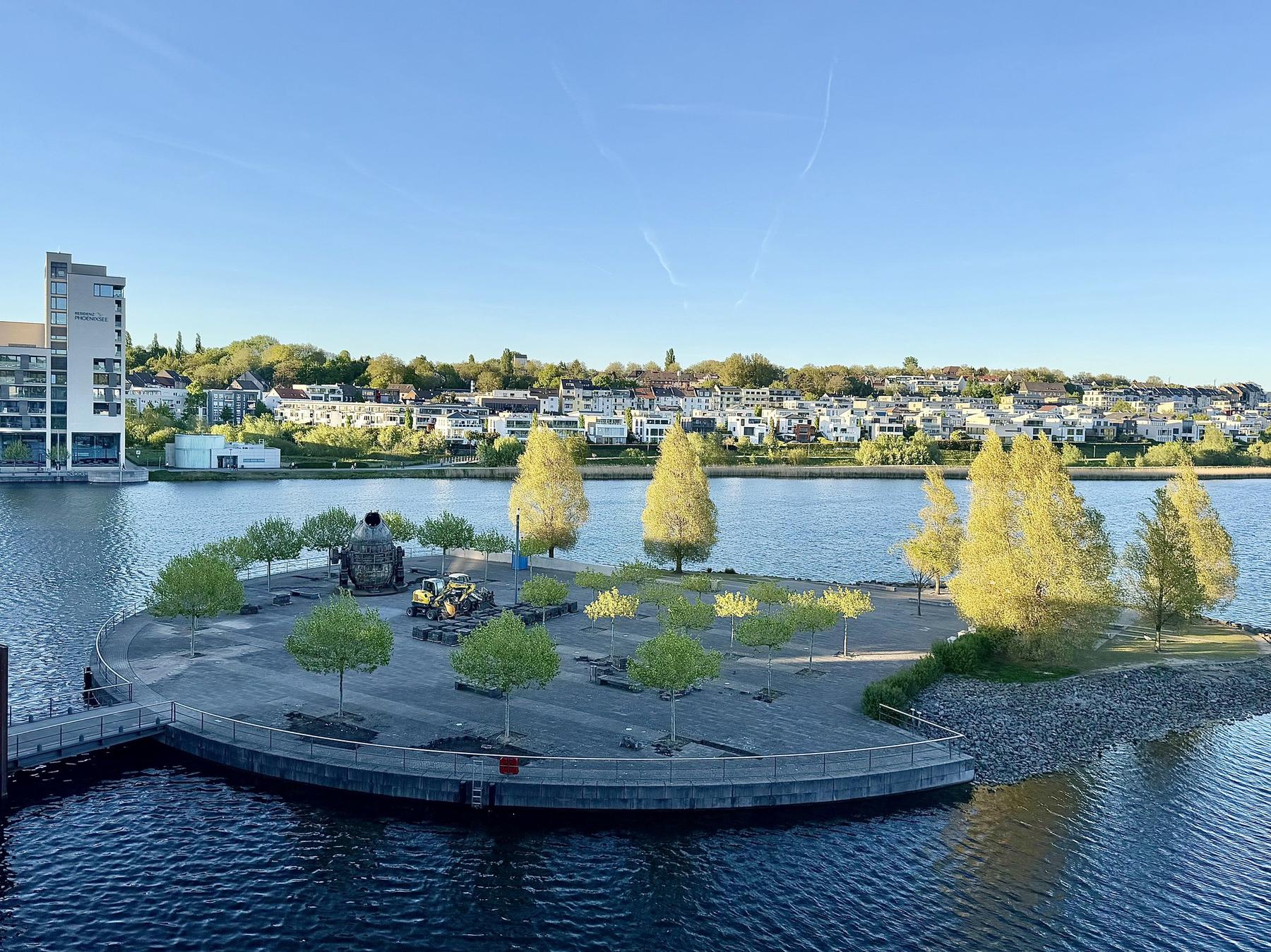 Phoenixsee Dortmund - Blick auf die Kulturinsel mit jungen Bäumen, dahinter die Hörder Wohnbebauung am Hang